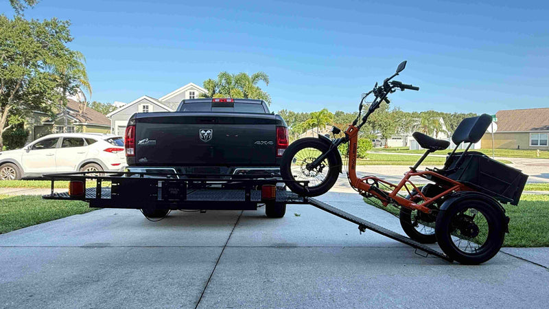 Black truck with a trailer attached carrying a three-wheeled vehicle on a driveway